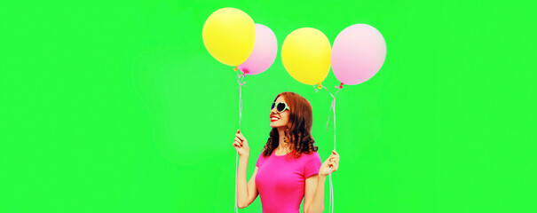 Summer colorful image of happy smiling young woman looking up with yellow pink balloons looking up at copy space on green background