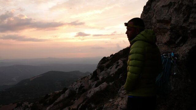 Young man with climbing gear looking at the horizon in the mountains.
