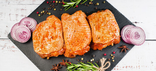 Three pieces of chicken thighs marinated in red sauce on a kitchen cutting board, on a light background, banner. Convenience food, quick cook, semi-cooked food.Top view.