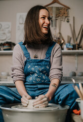 Smiling female potter working on pottery wheel while sitting in her workshop