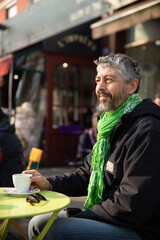 portrait d'un homme de 50 ans souriant qui prend son petit déjeuner à la terrasse d'un café au soleil. C'est un moment de détente. Une tasse de café et des croissants sont posés sur la table