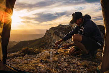 Man with cap cooking during a camping trip in the mountain.