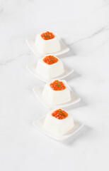 Mini Cream cottage cheese pudding in the shape of a square savarin, with red caviar, on a serving plate. Light background