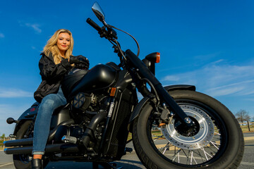 Fototapeta na wymiar A Lovely Blonde Model Enjoys The Outdoor Weather While Posing With Her Motorcycle