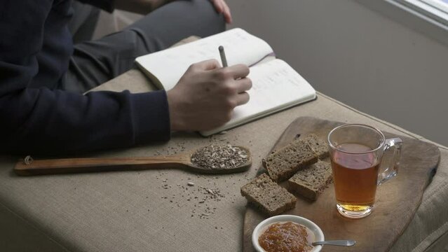 Man sitting at table and writing in notebook. On desk healthy breakfast and book note. Working house concept.