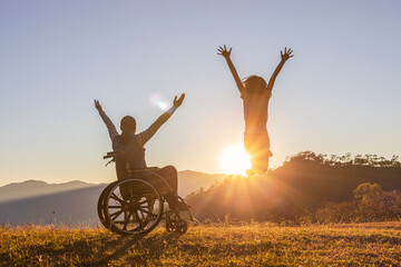 Disabled handicapped woman in wheelchair with raised arms and children jumping at sunset. happy...