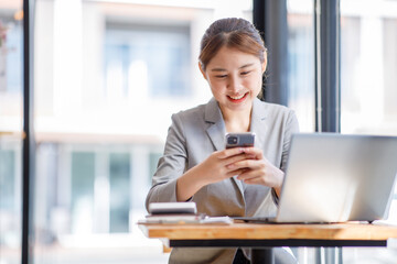 Portrait of an attractive Asian young woman holding her smartphone while working in a coffee shop.