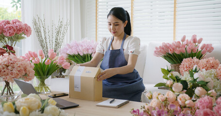 Asia people SME owner young woman smile enjoy selling prepare sale order product wrap flower gift box carton send parcel by post service. Happy freelance job work at home in digital modern store shop.