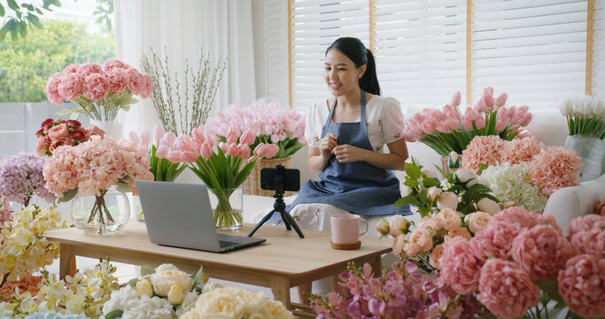 Asia girl vlogger influencer or SME owner people smile work on home video camera selfie shoot filming for live sell show happy talk on mobile VoIP app. Remote sale product at modern florist gift shop.