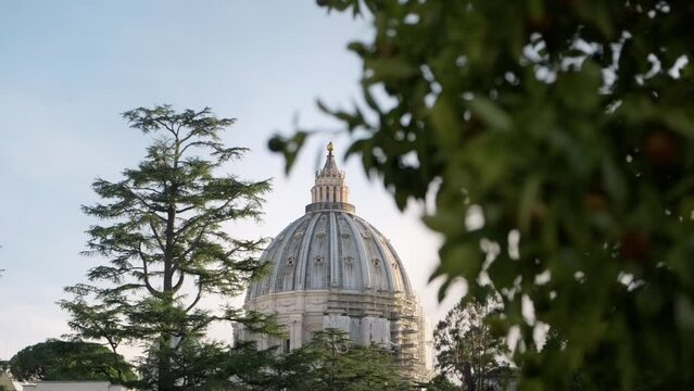 Rack focus on Saint Peter Basilica church dome at sunset from the Vatican Gardens.