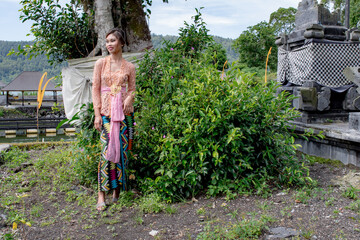 Young Balinese girl dressed in colorful batik sarong poses in front of a temple, Bali, Indonesia 