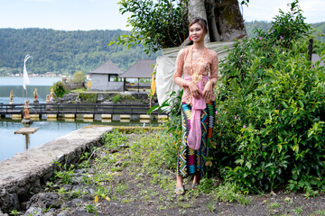 Young Balinese girl dressed in colorful batik sarong poses in front of a temple, Bali, Indonesia 