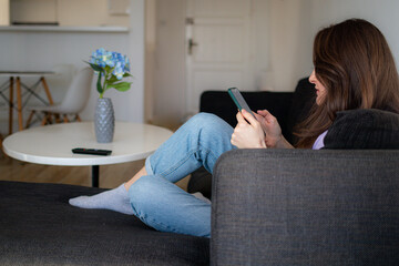 A young woman is sitting on a sofa and using her cellphone