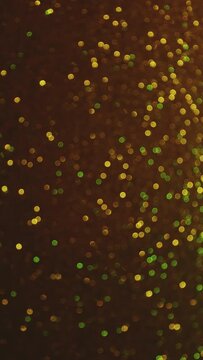 Bokeh vertical background of gold colors. Fast changing tiny green circles on dark back. Holidays New Year St Patrick's day and party concept with copy space.