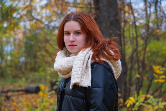 portrait of a red - haired smiling girl in a jacket smiling . against the background of autumn nature, the concept of human emotion