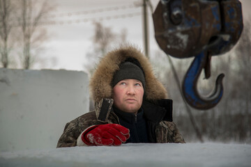 Portrait of a fitter in a winter jacket at the hook of a truck crane