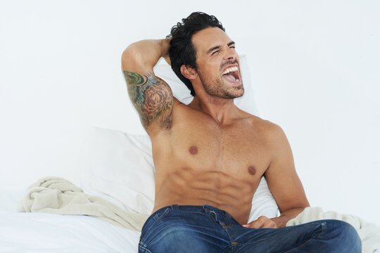 Early riser. Shot of a bare-chested young man sitting on his bed and yawning.
