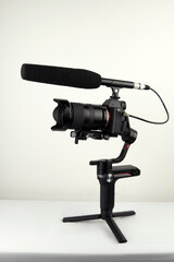 mirrorless camera and a connected microphone mounted on an electronic stabilizer on a white background
