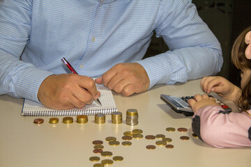 Hands of a dad and daughter teaching how to count money. Row of pennies and calculator on the table