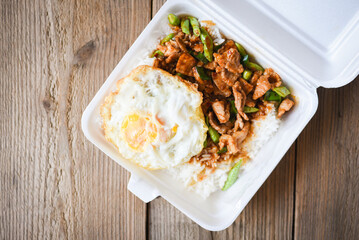 Stir fried pork with red curry paste and basil leaves with yardlong bean and fried egg topped in a plastic box, Thai street food or food delivery
