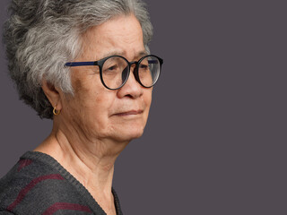 Senior woman looking away with face serious while standing on gray background