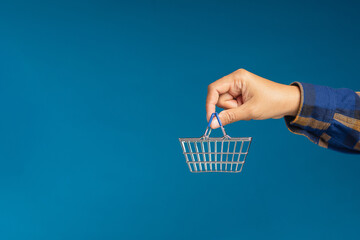 Close-up of hand holding an empty mini shopping cart over a blue background