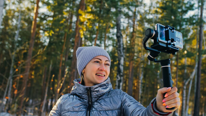 Woman Holding On Handheld Film 3-axis Gimbal Stabilization Device in Winter for Smartphone. Girl Blogger Make Selfie, Broadcast Video Blogging, Vlogging. Videographer Operator Take Photo Video.