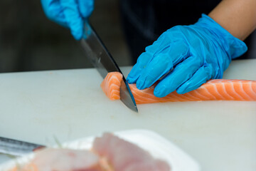 The salmon is in the hands of the experienced  chef. She is using a knife to slice salmon fillet for sashimi and sushi. A chef cutting a salmon fillet with a knife on a cutting board. Cut fish fillet 