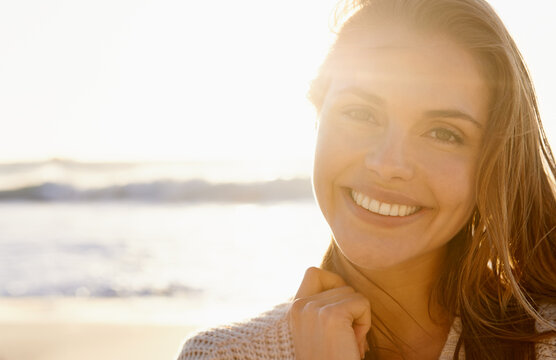 Stunning smile at sunset. A pretty young woman smiling confidently as the the sun sets on the beach in the background.