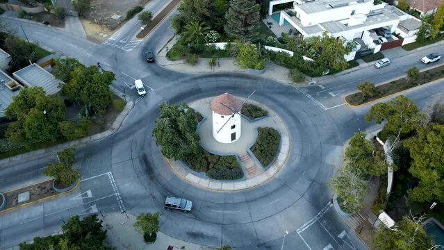 Aerial orbit of Leonidas Montes windmill tower in roundabout with cars driving surrounded by trees, Lo Barnechea, Santiago, Chile