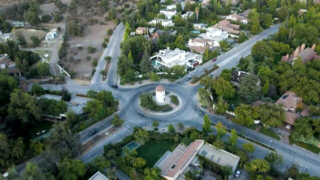 Aerial dolly in lowering on Leonidas Montes windmill tower in roundabout with cars driving surrounded by trees, Lo Barnechea, Santiago, Chile