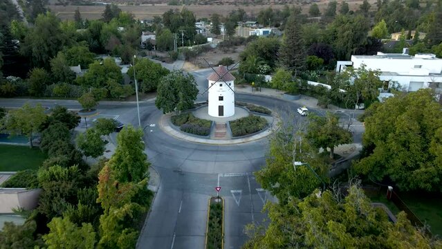 Aerial dolly out of Leonidas Montes windmill in roundabout with cars driving surrounded by trees, hills in background, Lo Barnechea, Santiago, Chile