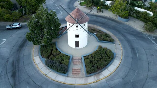 Aerial dolly out of Leonidas Montes windmill tower in roundabout with vehicles driving surrounded by trees, Lo Barnechea, Santiago, Chile
