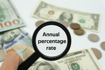 Magnifying glass showing the words "Annual percentage rate".Background of banknotes and coins.basic concepts of personal finance.