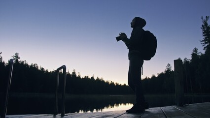 Silhouette traveler photographing scenic view in forest, river. Wood pier. One woman shooting nice...
