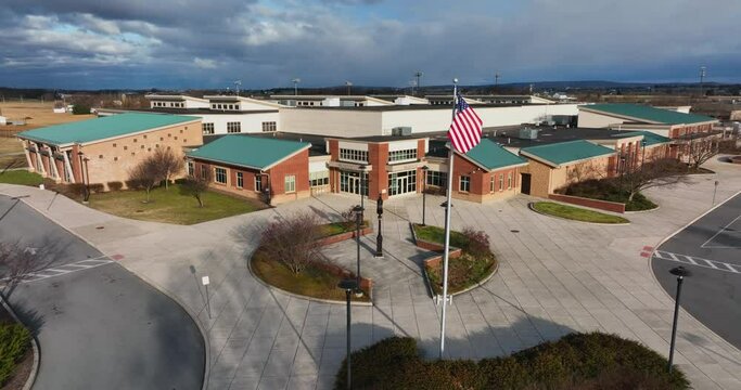 Modern school building in USA. American flag at entrance of education campus in winter morning light. Aerial establishing shot.