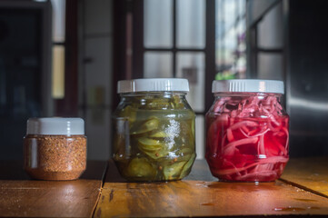Pickles of cucumber and red onion in a glass bowl, wooden table and door open in the background