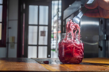 Pickles of cucumber and red onion in a glass bowl, wooden table and door open in the background