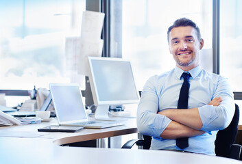 Obraz premium Its a great day to be doing business. Portrait of a smiling businessman sitting at his desk with his arms crossed.