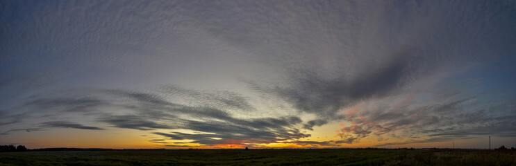 Panorama of a flat landscape with dark clouds at sunset