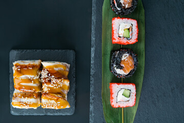 close-up, on a dark table, top view, Japanese rolls with eel, salmon, cucumber and cream cheese on a bamboo leaf