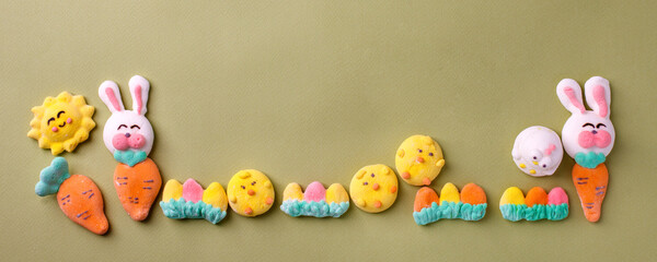 Obraz premium Happy Easter concept. Preparation for holiday. Easter marshmallow candy chiken, rabbit, carrot, bunny on green pastel background. Simple cute, funny minimalism flat lay top view, copyspace banner