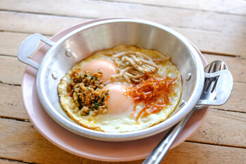 Pan-fried eggs with toppings on the wooden table.