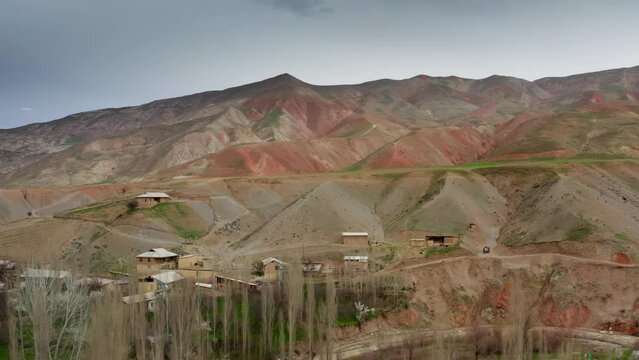 A beautiful landscape of mountain villages of Tajikistan in springtime taken from a drone. Residential buildings located at the foot of sandstone mountains shot through spring trees without leaves. 