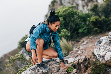 Naklejka na ściany i meble Smiling woman climbing up on a mountain. Female hiker sitting on a stone.