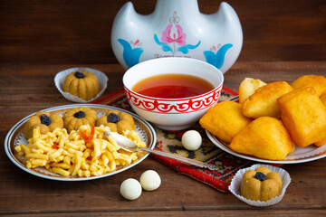 Kazakh still life on Nauryz, with national food: baursaks, zhent, kurt, chak chak and tea on a wooden background