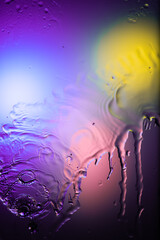 drops and splashes of water spreading on glass on a bright colored background