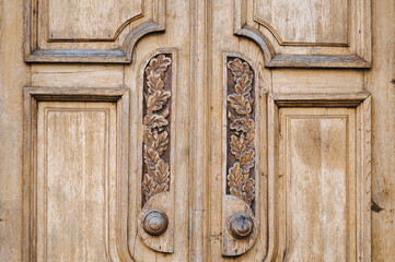 Light brown wooden door with decorative carvings in the form of a column and a flower in a circle of larch or oak. Vintage background from natural material.