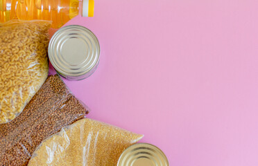 Various canned food, pasta, cereals and sugar on a pink background. Humanitarian food aid to people...