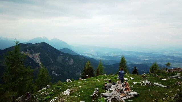 An active hiking couple having a rest with a panoramic lookout from from Hochpetzen in the Karawanks in Carinthia, Austria. Aerial view on the valley and the surrounding mountains. Aerial photography
